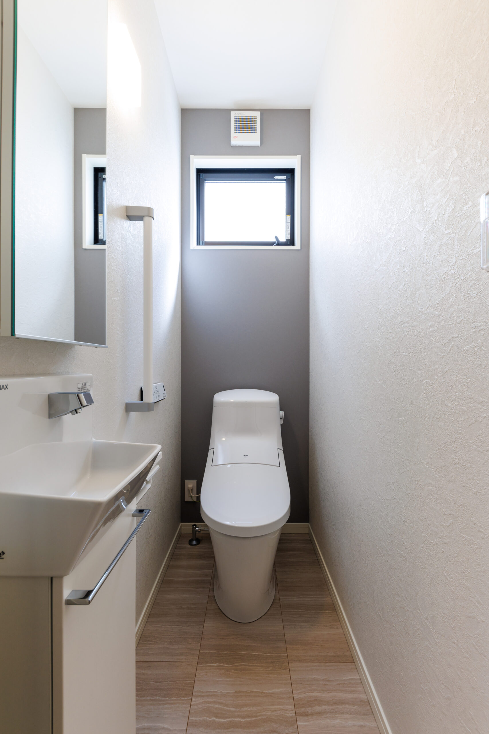 T-2／背面のグレーのアクセントウォールが、落ち着いた上質な空間を演出するトイレです。手をかざすだけで水が出る、衛生的で便利な自動手洗い器を備えています。